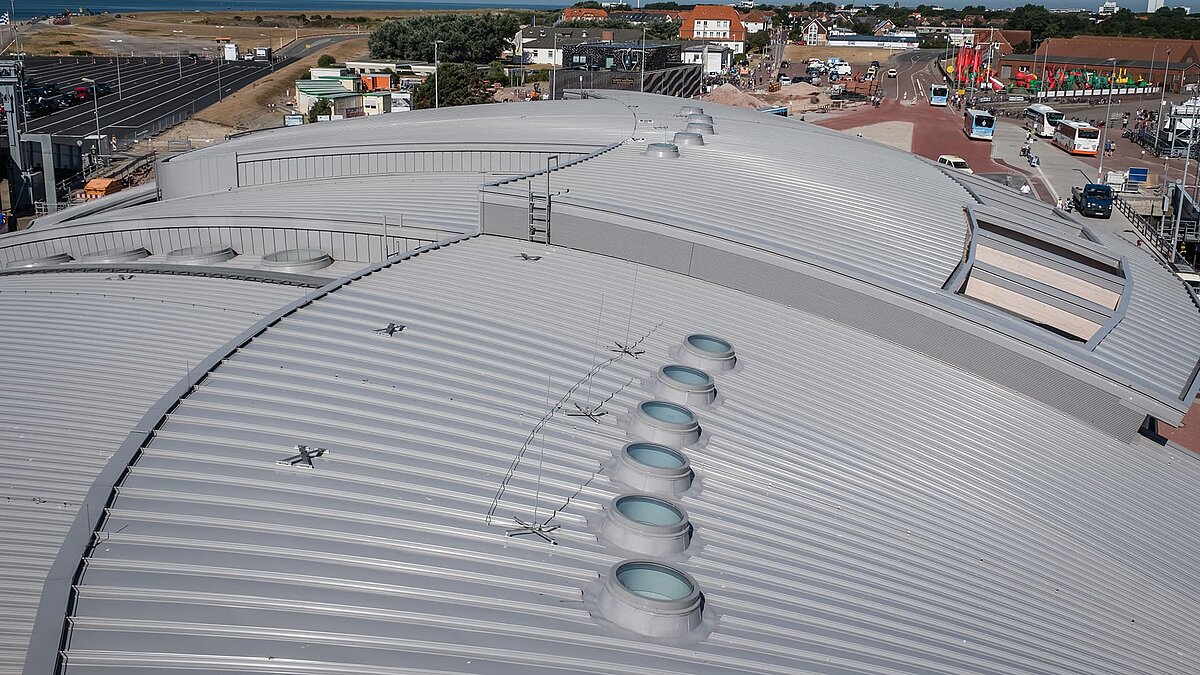 Roof of the Norderney harbour terminal with round flat roof windows and undulating metal construction.