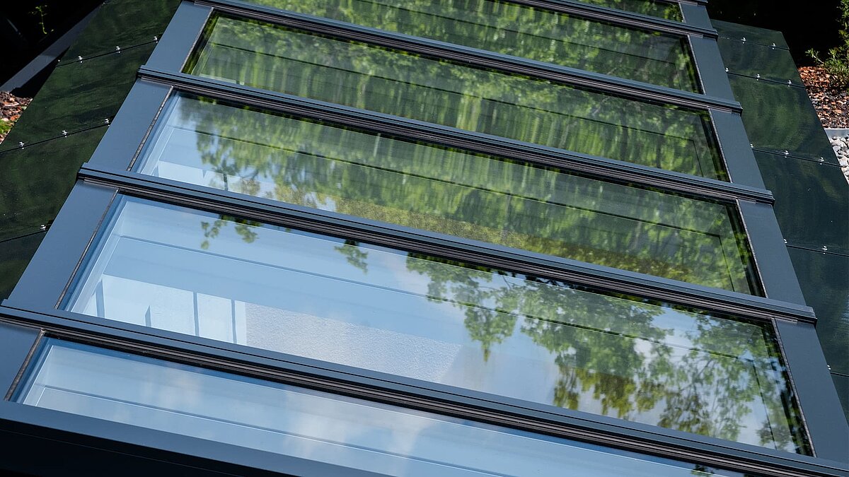 Close-up of a modular glass roof by LAMILUX in a residential building in Freiburg, reflecting trees in the glass panels.