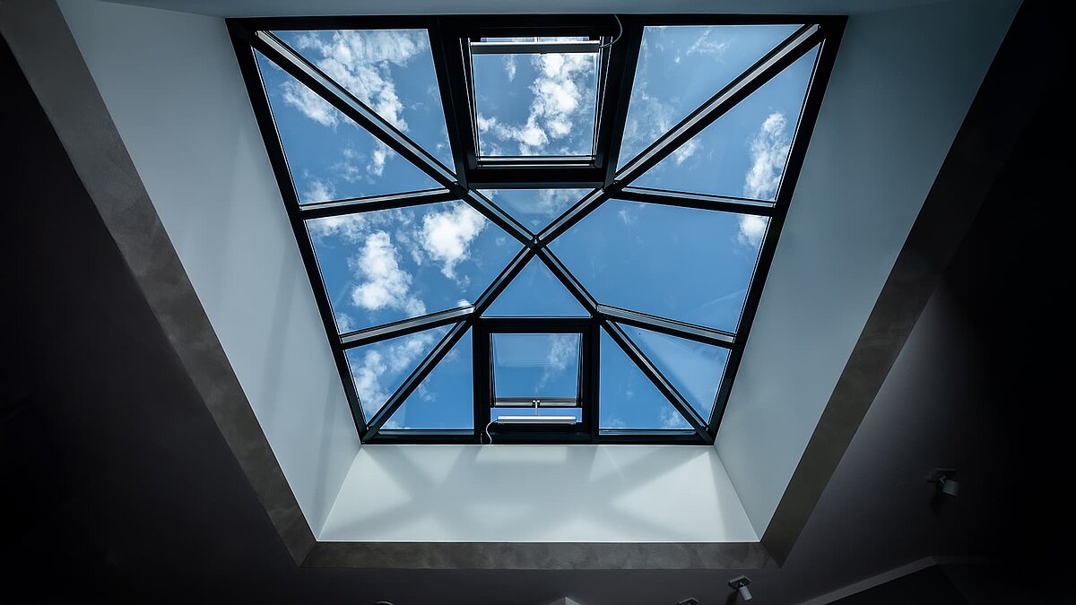 Interior view of a modern glass pyramid in a single-family home in Wichmannsdorf, reflecting the sky and clouds.
