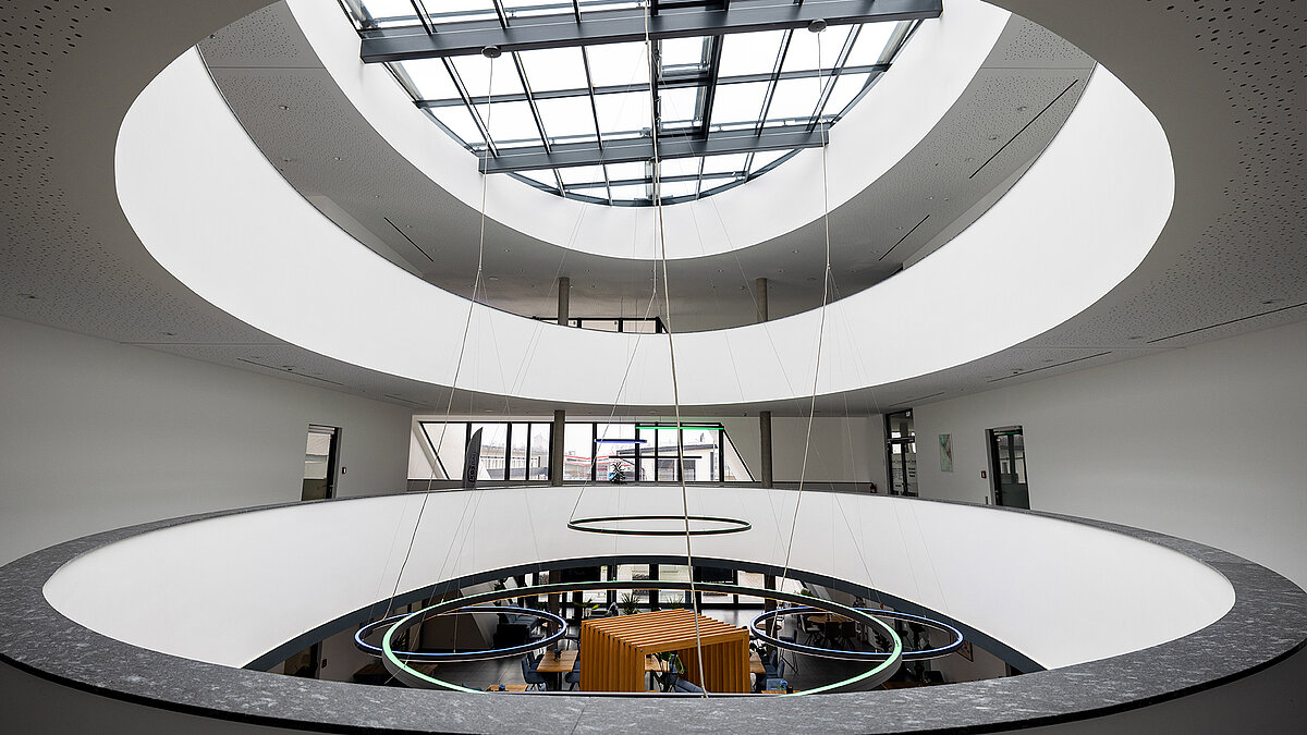 Modern atrium with oval atrium and glass roof, round LED lights and open view of the work area on the first floor.