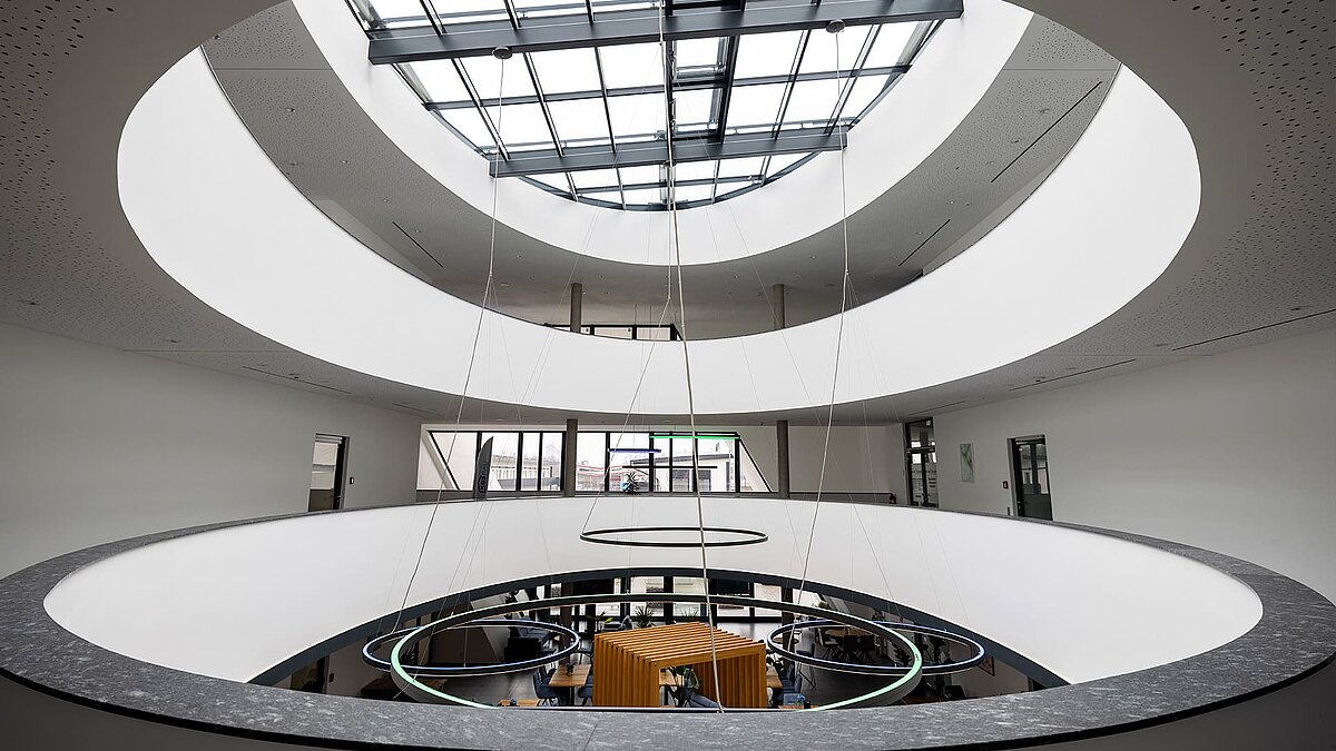 Modern atrium with oval atrium and glass roof, round LED lights and open view of the work area on the first floor.