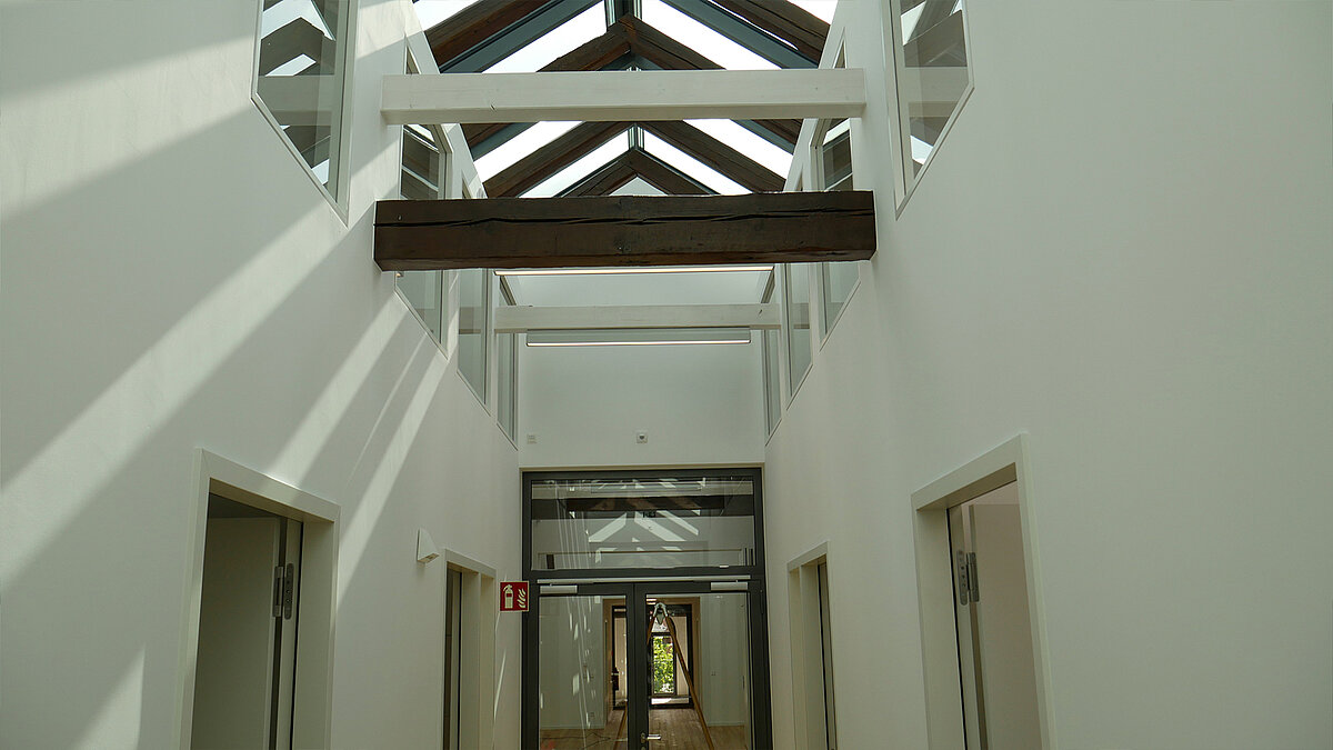 Sunlit corridor of Leibniz University Hannover with glass roof and exposed wooden beams.