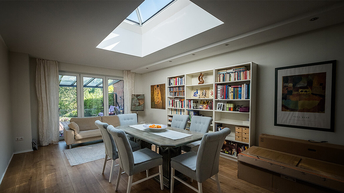 Living and dining room with a large skylight, a dining table, bookshelves and a view of the garden.