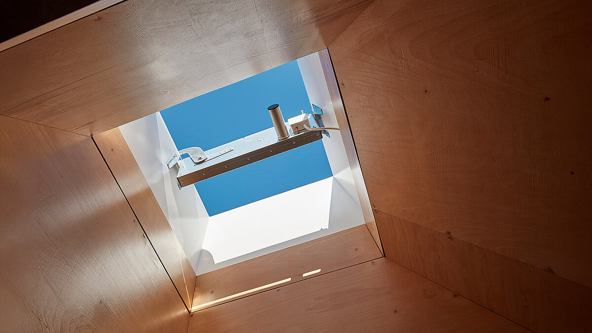 Square flat roof window in wooden ceiling with view of blue sky