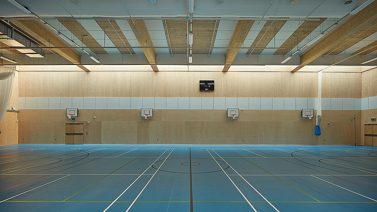 Sports hall at Harris Academy Sutton featuring timber ceiling beams, multi-purpose court markings and basketball hoops