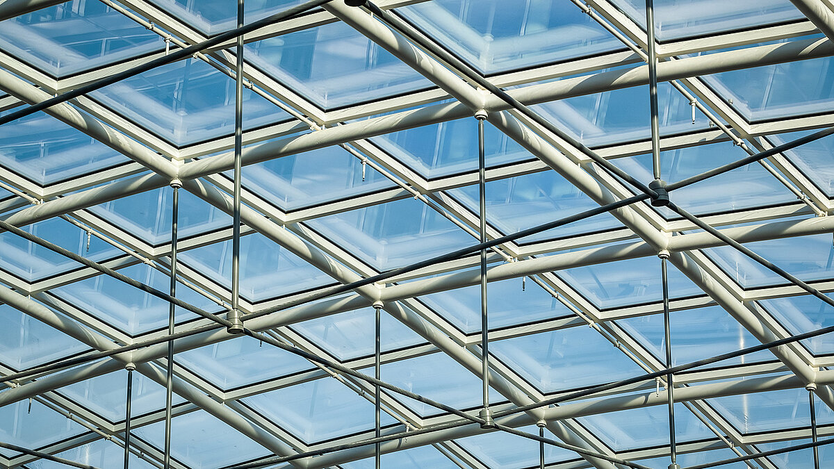 Glass roof of the Newton office building of the TÜV Süd Group with metal beams and blue sky in the background.