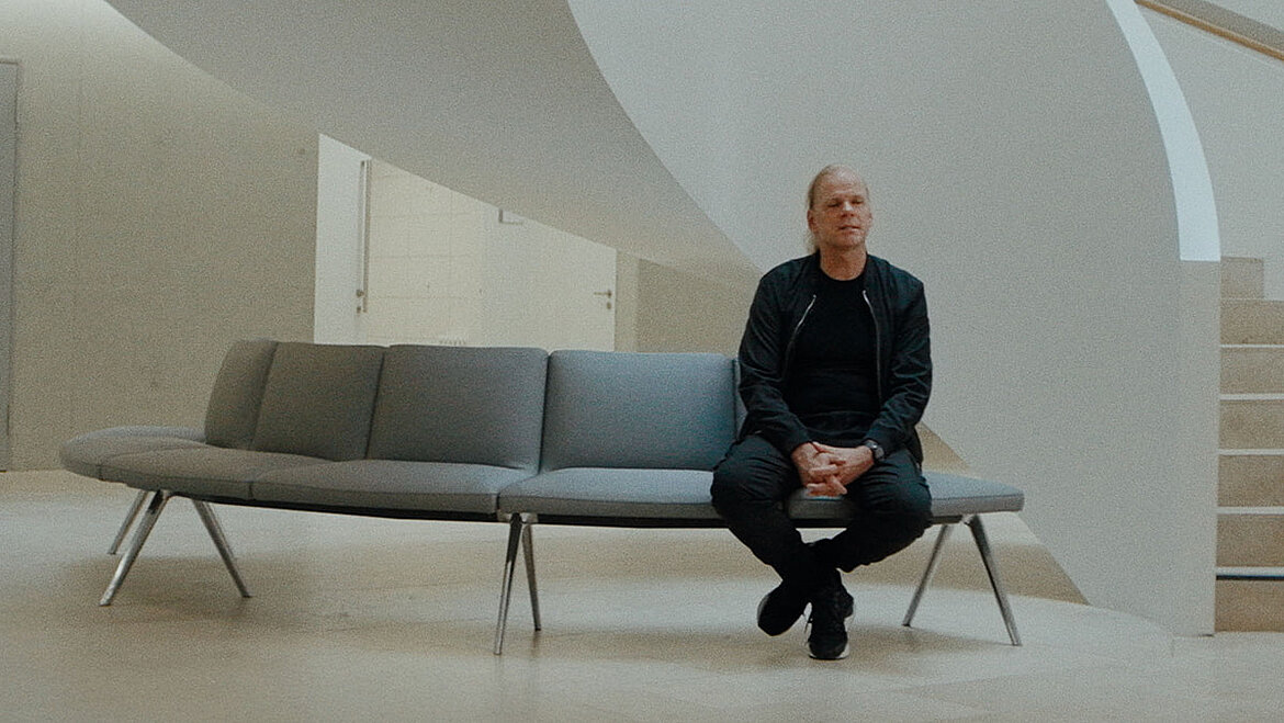 Person sitting on a bench in a modern interior space with an organically shaped wall and calm, minimalist architecture