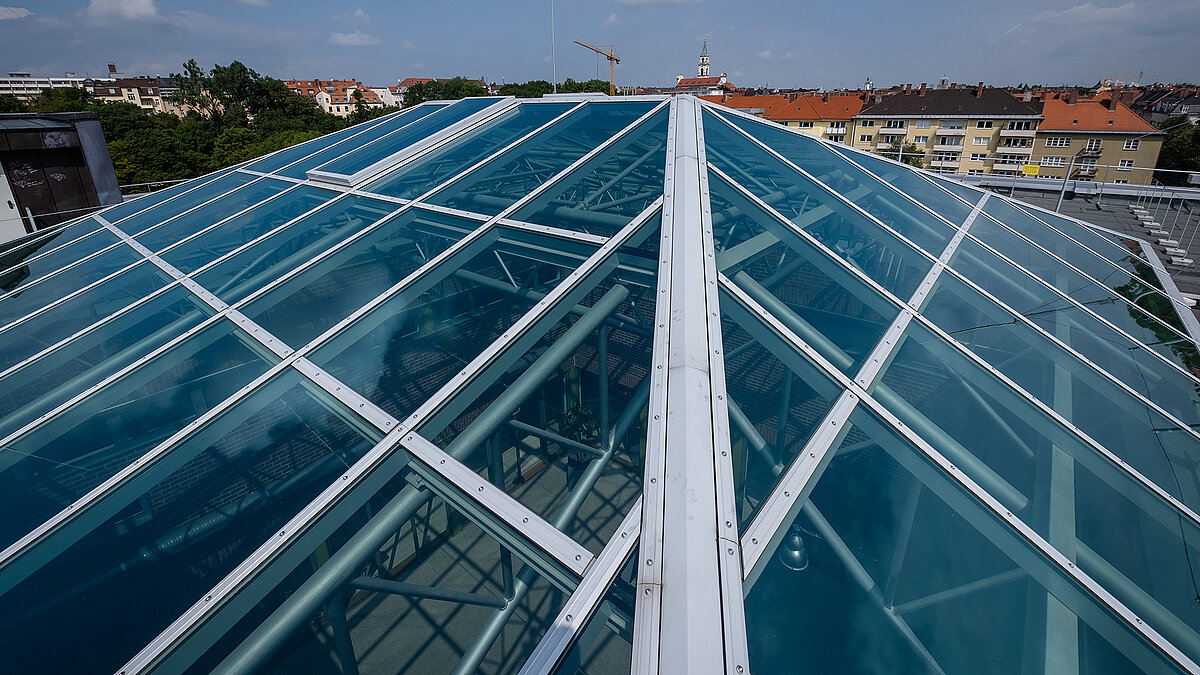 Close-up of the glass roof of the Dante-Gymnasium with blue glazing and sturdy steel structure, visible pipes and beams underneath.