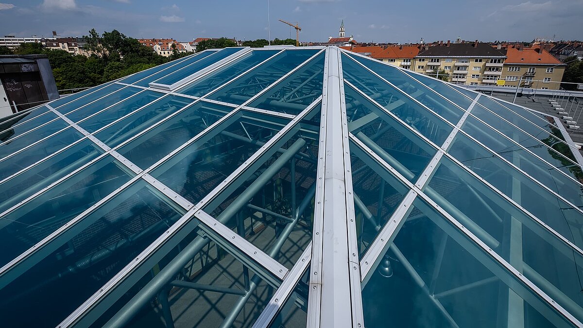 Close-up of the glass roof of the Dante-Gymnasium with blue glazing and sturdy steel structure, visible pipes and beams underneath.