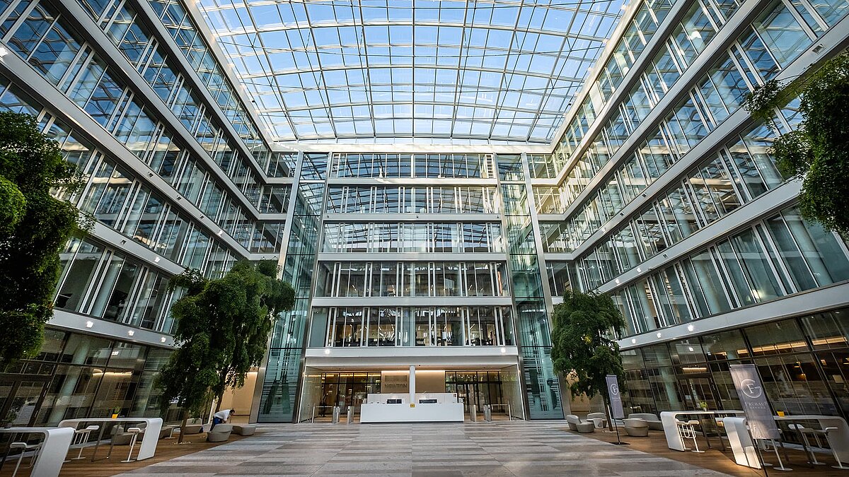 Interior view of the Newton office building of the TÜV Süd Group with a modern glass roof, large windows, and a green atrium.