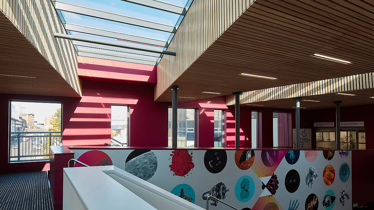 Interior of Sheffield Hallam University featuring LAMILUX PR60 glass roof, modern wooden elements, and colorful wall design.