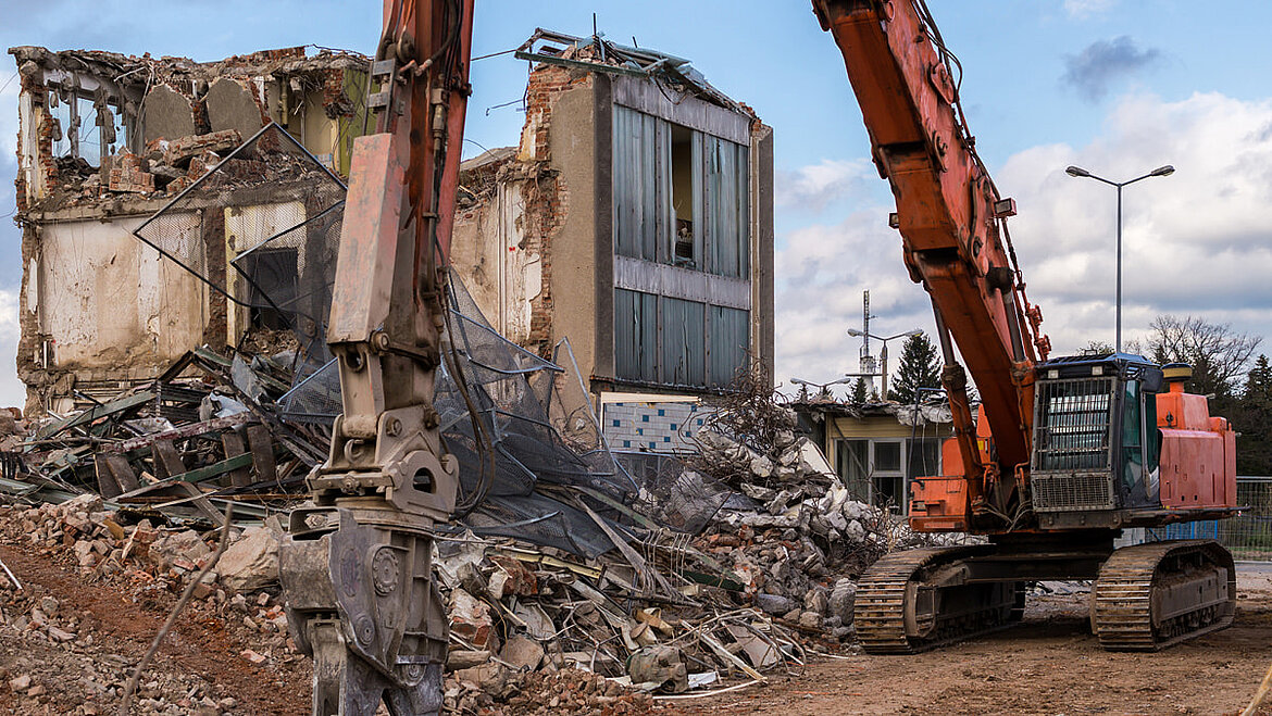 Excavator demolishing an old building surrounded by rubble