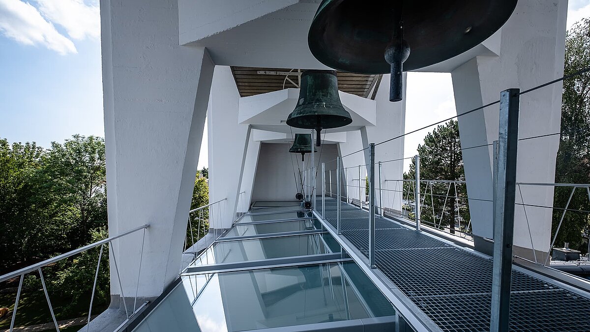 Bell tower of Pauluskirche in Traunreut featuring LAMILUX flat roof windows FE and a metal walkway.