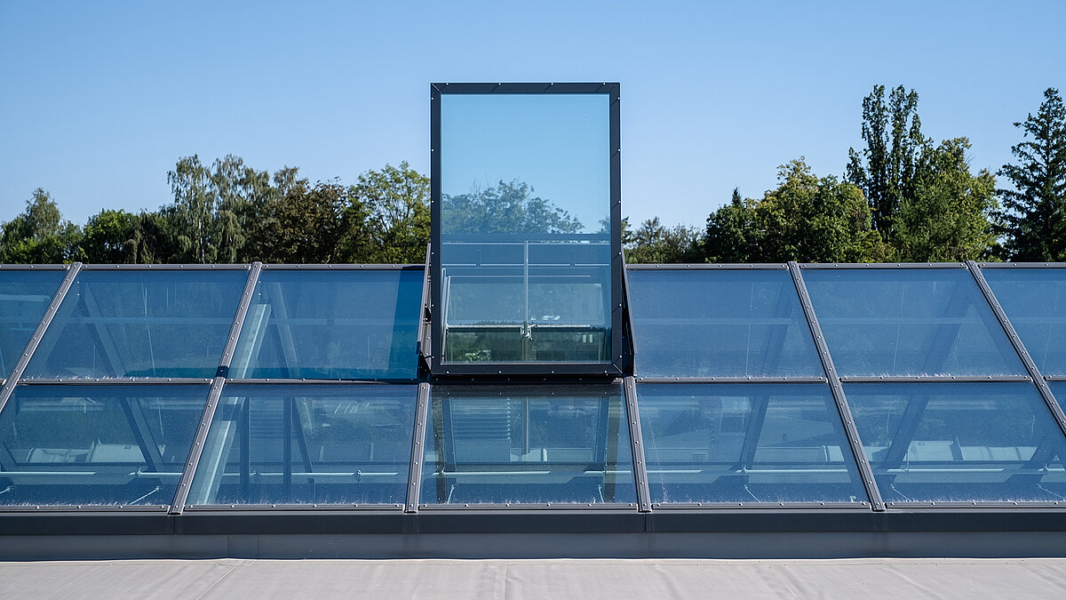 Glass roof with flat roof exit at the Outlet Center Selb, surrounded by trees.