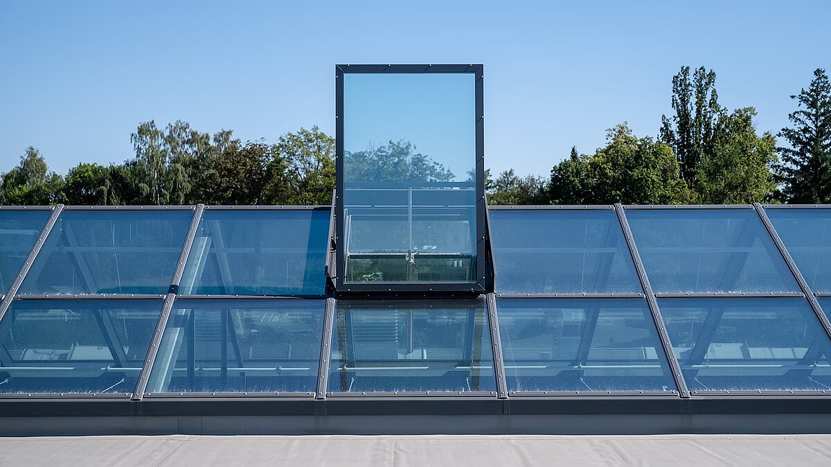 Glass roof with flat roof exit at the Outlet Center Selb, surrounded by trees.