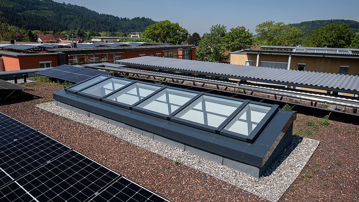 View of the modular glass roof from LAMILUX from the residential building in Freiburg surrounded by solar panels on a green flat roof.