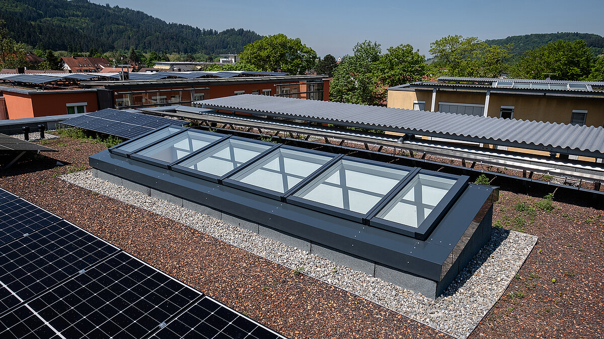 View of the modular glass roof from LAMILUX from the residential building in Freiburg surrounded by solar panels on a green flat roof.