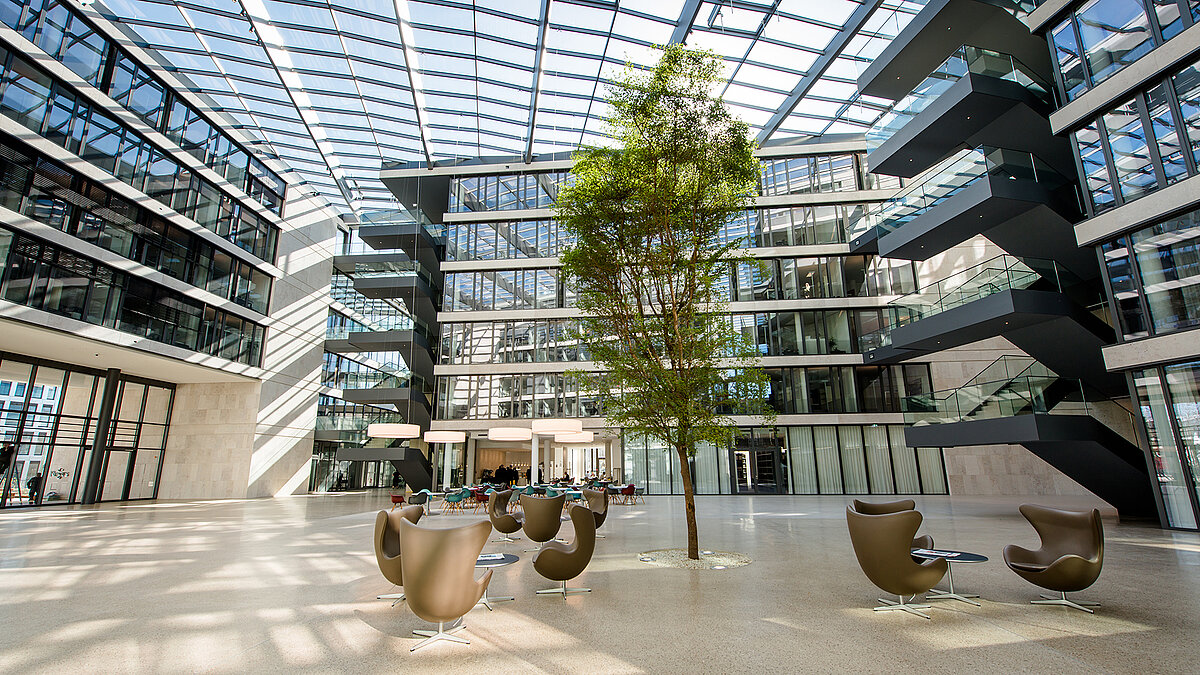 Atrium of the FGS Campus with glass roof, modern interior architecture, a central green tree area, and elegant seating arrangement.