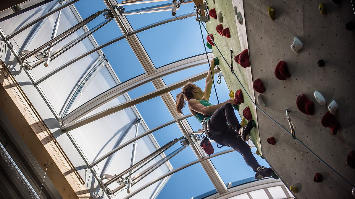 Female climber on an indoor climbing wall at the OWL climbing center under a large skylight providing natural daylight.