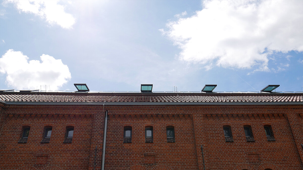 Brick facade of Leibniz University Hannover with glass roof elements on the rooftop under a blue sky.