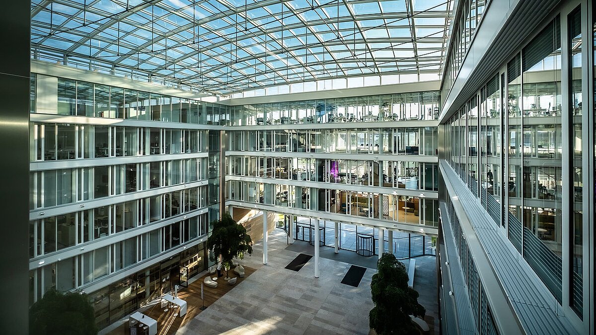 Modern atrium of the Newton office building of the TÜV Süd Group with a glass roof and large glass facades.