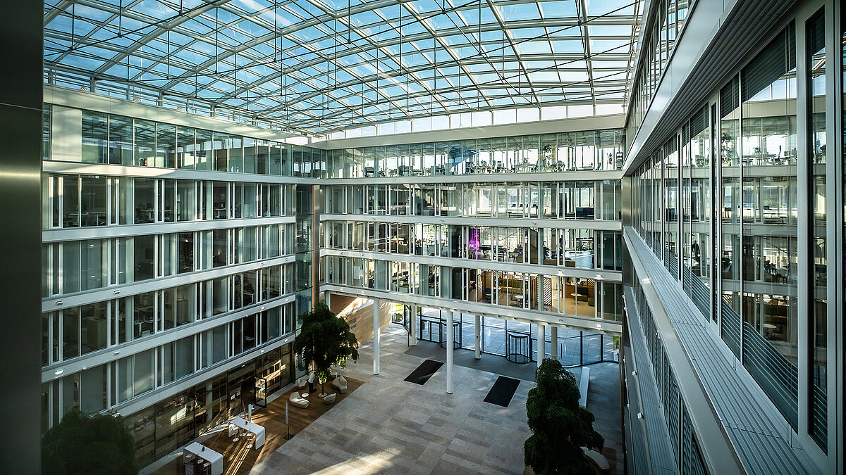 Modern atrium of the Newton office building of the TÜV Süd Group with a glass roof and large glass facades.
