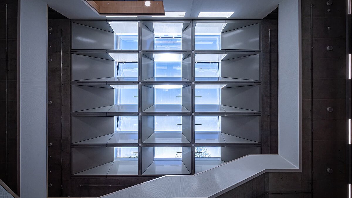 View looking up at a square glass roof with surrounding shelves in an interior space
