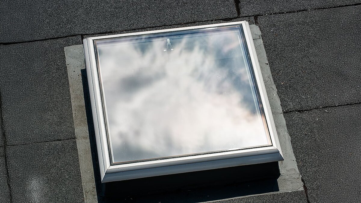 Closed flat roof window reflecting the sky on a grey roof at Caritas Hagen.