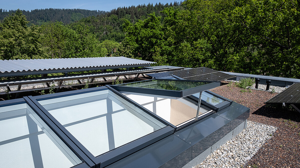 Residential building in Freiburg with a modular glass roof by LAMILUX, partially opened, surrounded by solar panels and a green flat roof.