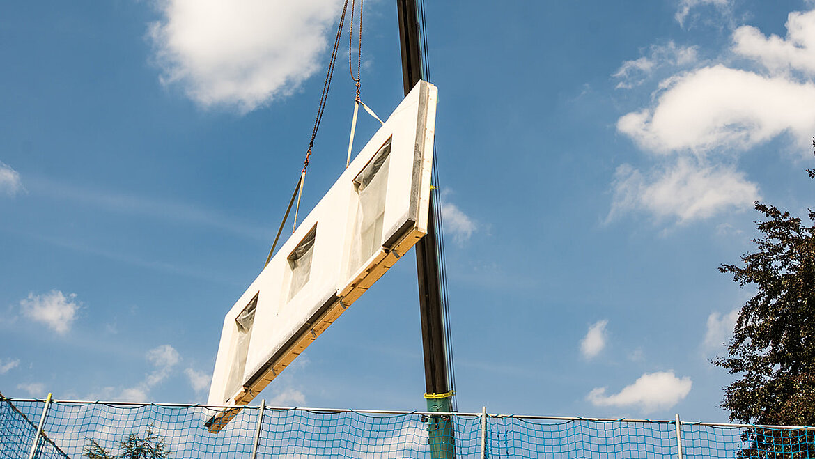 Component of a modular house on a crane Modular construction wall with GRP facade panel suspended by crane | insights by LAMILUX