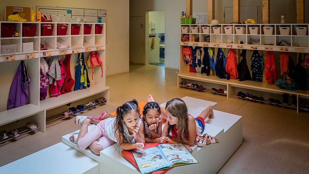 Daylight supports children in their development Children lie in the light-flooded kindergarten and read a book together | insights by LAMILUX