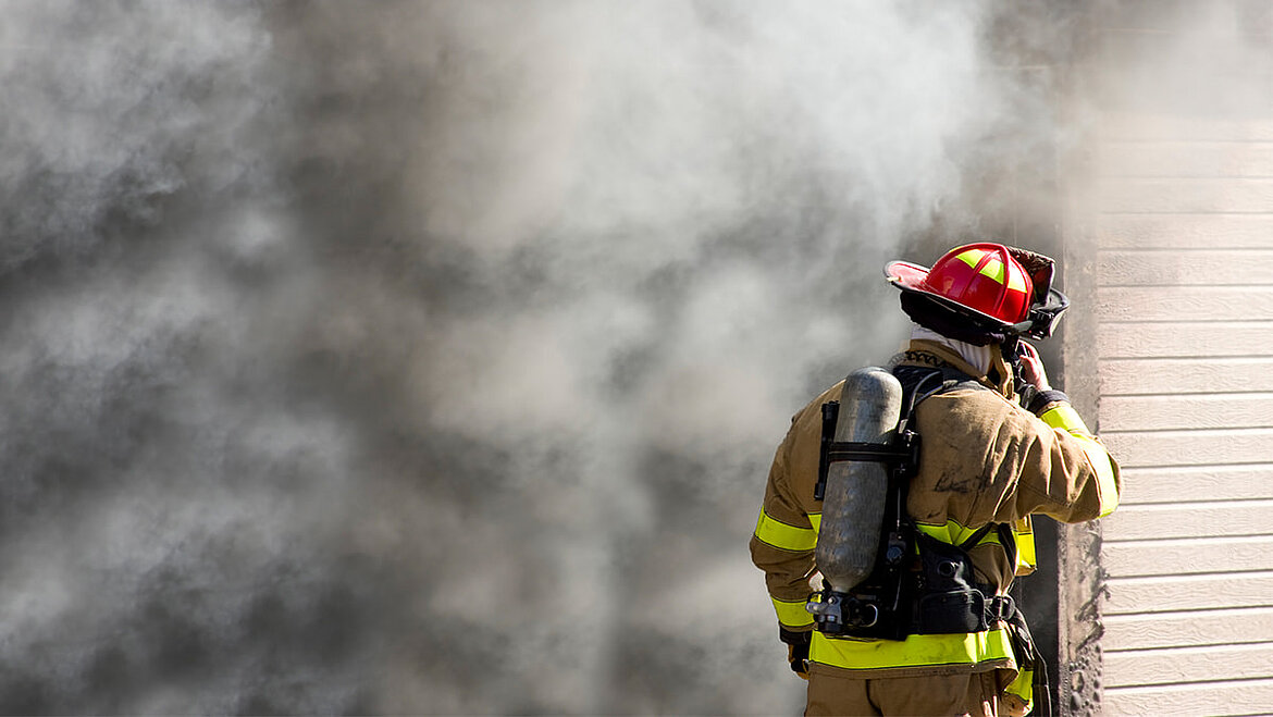 Fire smoke is the greatest source of danger in a fire. Firefighter in front of burning building with fire smoke | insights by LAMILUX