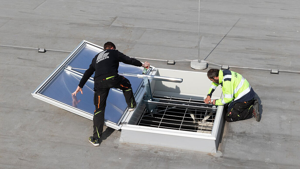 Two people building an open rooflight dome on the roof | insights by LAMILUX