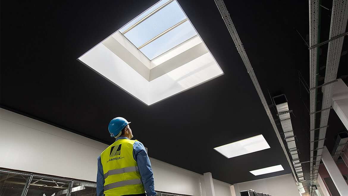 The F100 smoke lift from LAMILUX opens in the event of a fire and allows smoke to flow out of the building. Man inspects smoke lift in hall | insights by LAMILUX