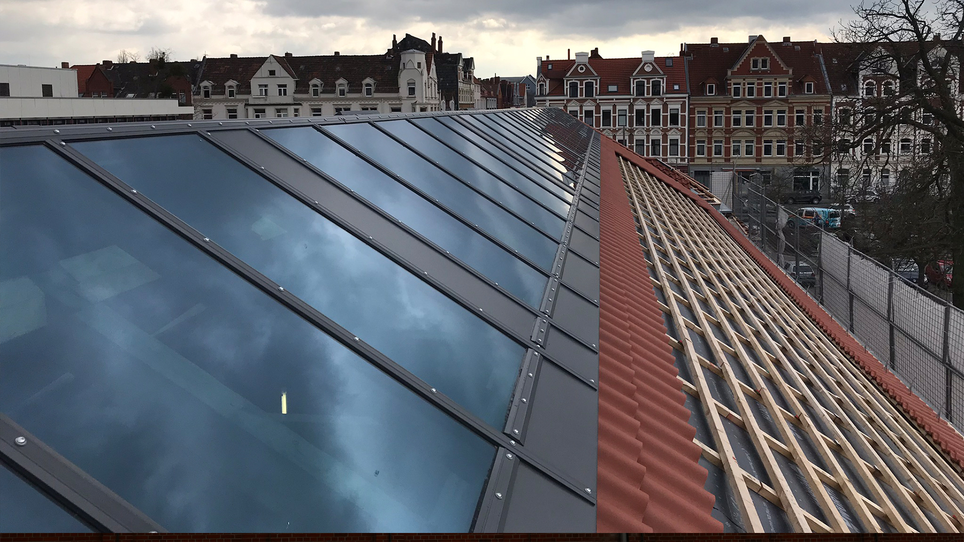 Modern glass roof with a red tiled roof in the construction phase at Leibniz University Hanover, with historical buildings in the background.