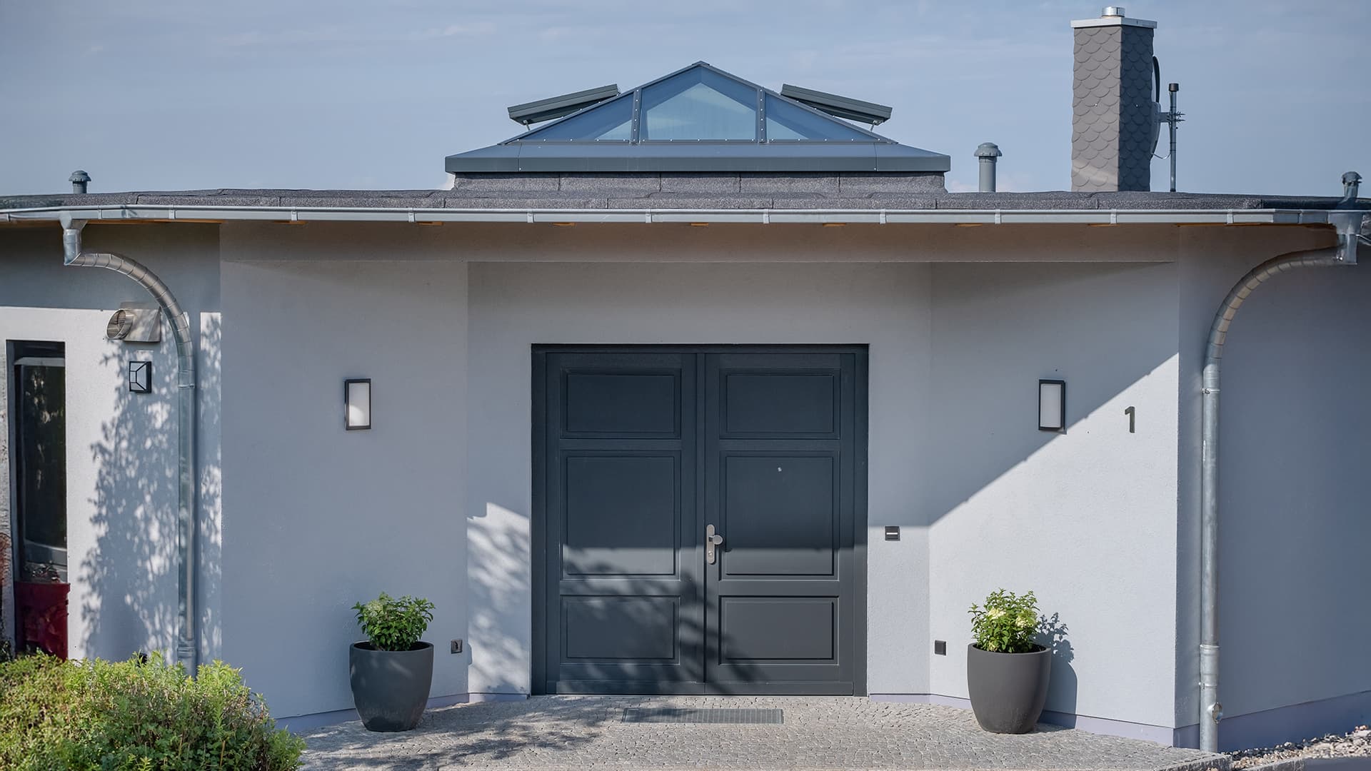 Modern entrance facade of a single-family home in Wichmannsdorf with dark gray double door and glass pyramid on the roof.