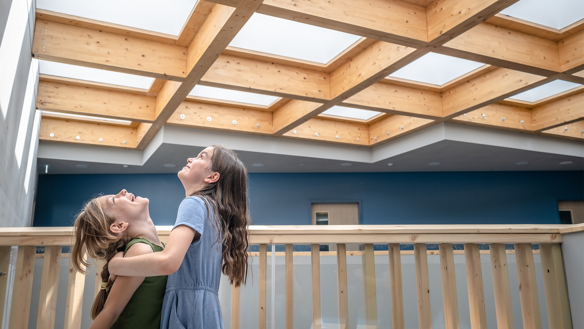 Two girls are standing on a wooden balcony, looking up at the ceiling 