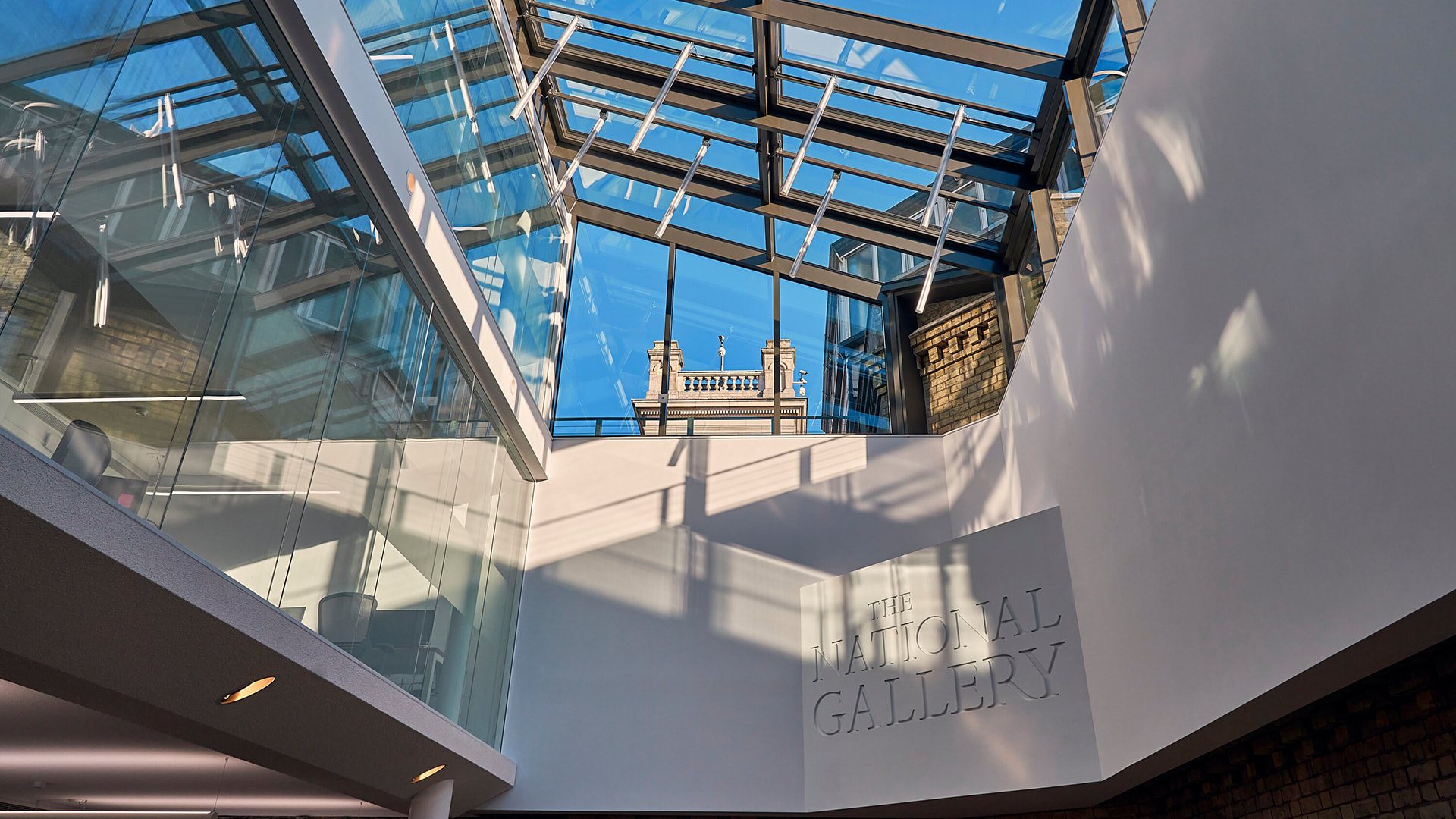 View upwards to a glass roof with white painted walls and brick facade